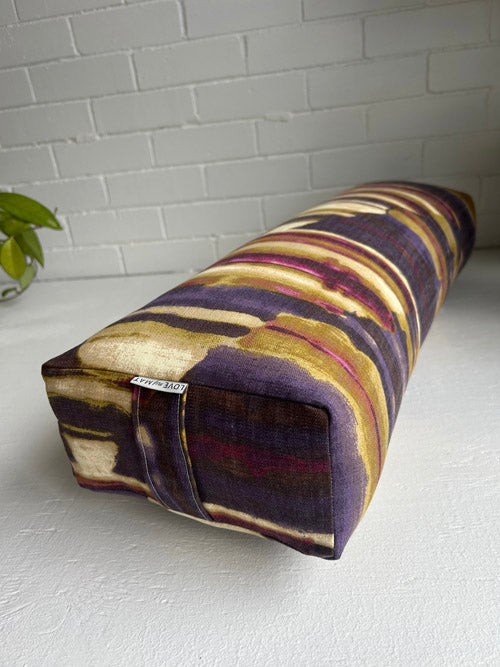 Striped abstract fabric bolster on a white surface with a white brick wall background