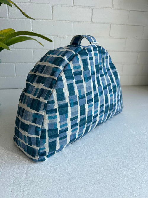 Blue and white checkered meditation cushion made in Canada on a white surface with a white brick wall background