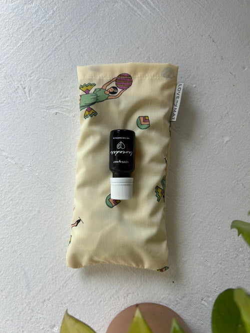 lavender oil bottle on top of retro fabric eye pillow on a patterned beige pouch against a light gray background