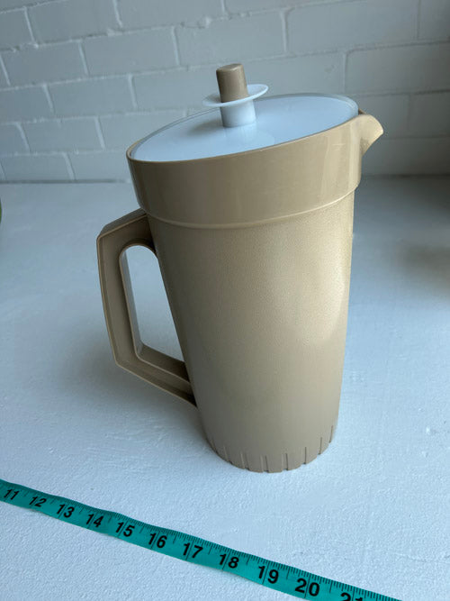 Beige pitcher with a white lid on a white surface, with a measuring tape for scale.