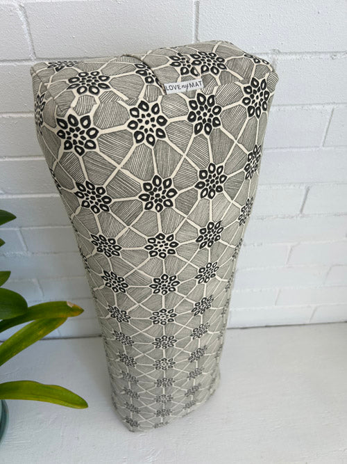 Cream and black fabric Yoga bolster with geometric pattern on a white surface and tiled wall background