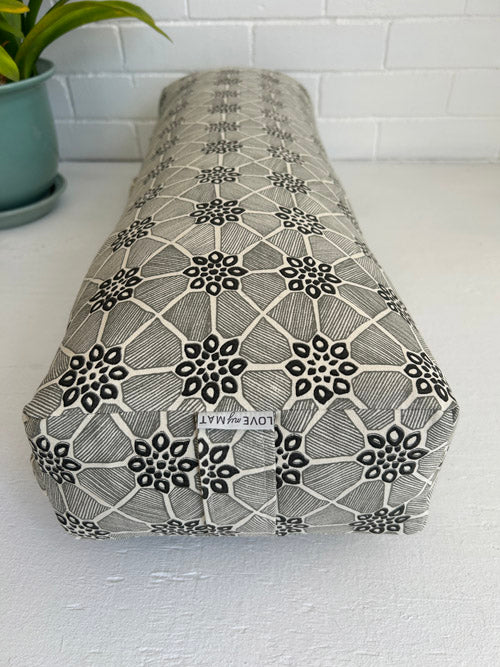 Rectangular fabric-covered yoga bloster with black floral pattern on a white surface.