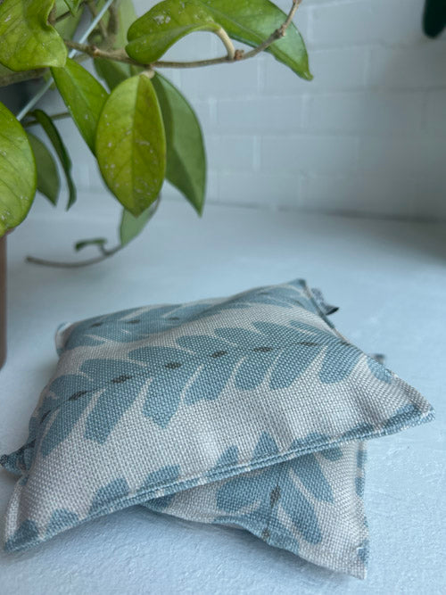 Textured fabric knee pillows with leaf pattern on a light surface, next to a plant.