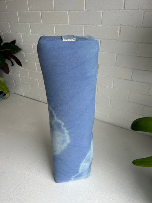 Blue yoga bolster t with white marbled pattern on a white surface with a light gray tiled wall background.