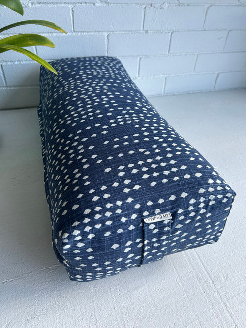 Blue and White modern print yoga bolster laying on a white surface and white background with a plant leaf near it.
