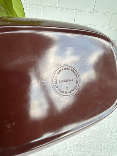 Melmac brand logo on a reflective surface with a blurred background