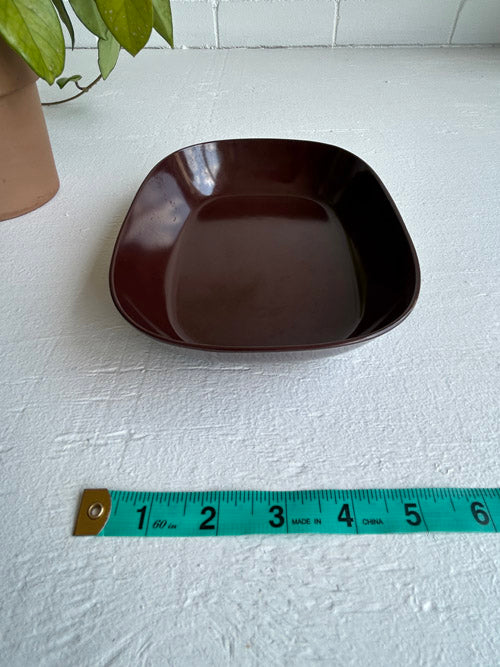 Brown ceramic bowl on a white surface with a measuring tape for scale.