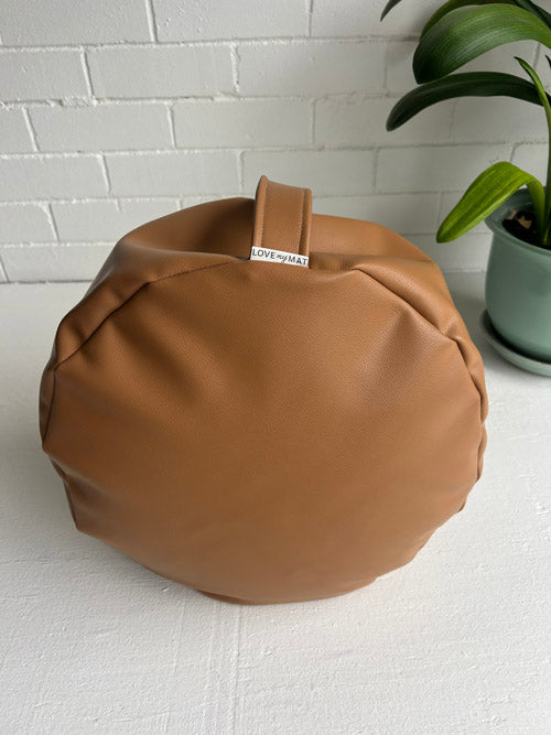 Brown floor cushion on a white surface with a plant in the background