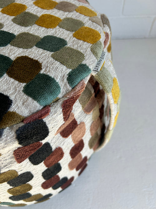 Colourful patterned fabric meditation cushion with a brand label on a white background