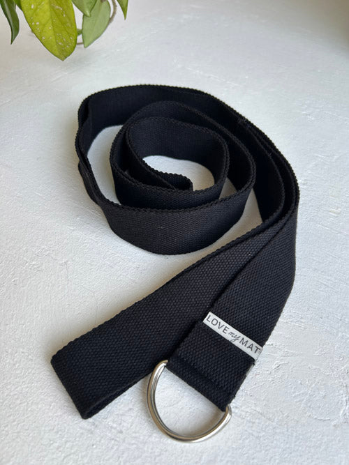Black yoga strap with a metal D-ring on a light background