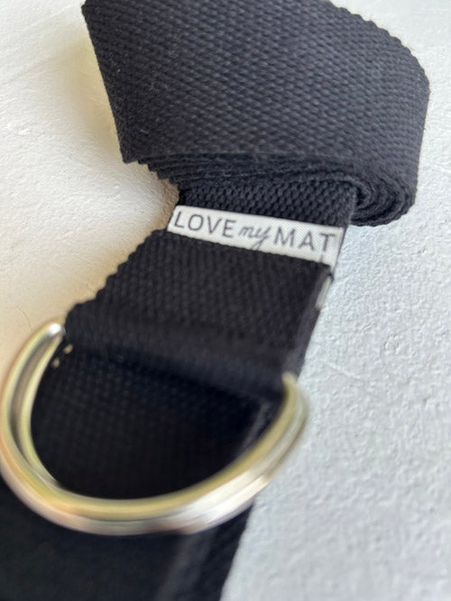 Black yoga strap with a metal ring on a light gray background