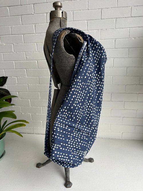 Mannequin wearing a navy blue fabric  yoga mat bag with white patterns against a white brick wall.