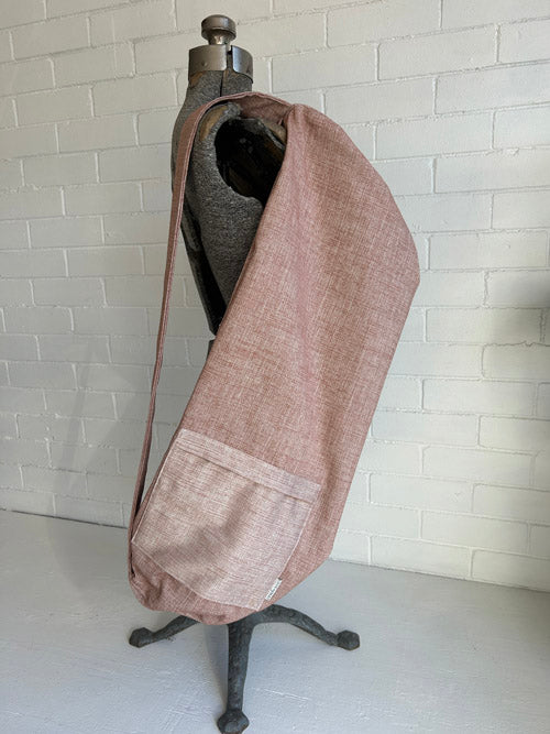 Mannequin wearing a brown/pink sling style yoga mat bag with a white trim against a tiled wall.
