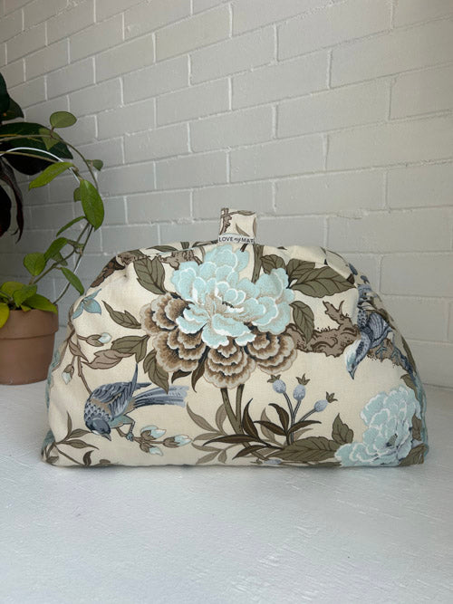 Floral-patterned fabric cover on a white surface with a plant in the background