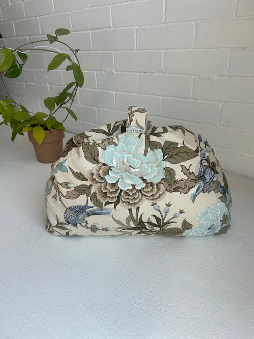 Floral-patterned fabric cover on a white surface with a plant in the background