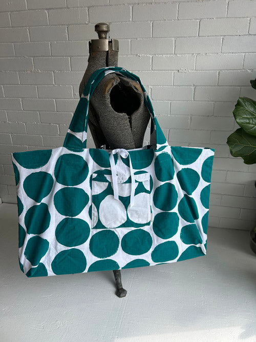 Green and white patterned tote bag on a mannequin against a white brick wall.