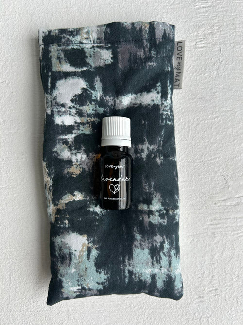 Bottle of lavender essential oil on an abstract patterned eye pillow against a white background