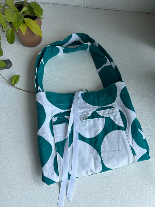Green and white patterned bag on a light surface with a plant in the corner