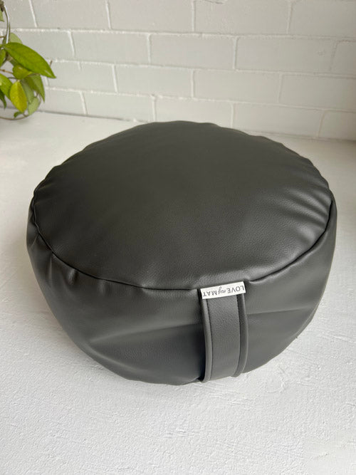Round dark grey vinyl floor cuhsion with a brand tag on a white surface.