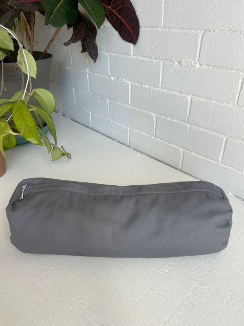 Gray fabric yoga bolster on a white surface with a plant in the background