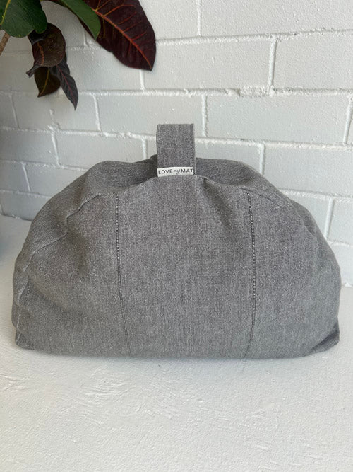 Gray fabric cushion with a strap on a white surface against a white brick wall.