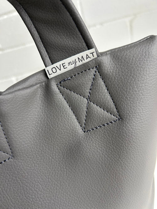 Close up of a vinyl sandbag with the tag "Love My Mat" with a white brick background
