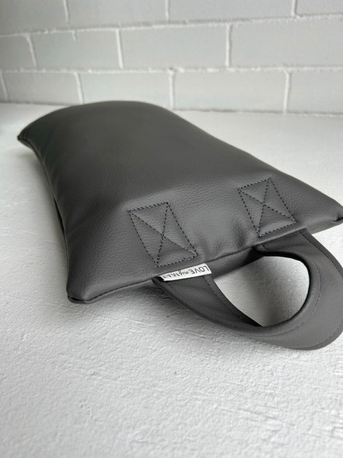 Grey Vinyl sandbag lying down on a white surface and a white brick background