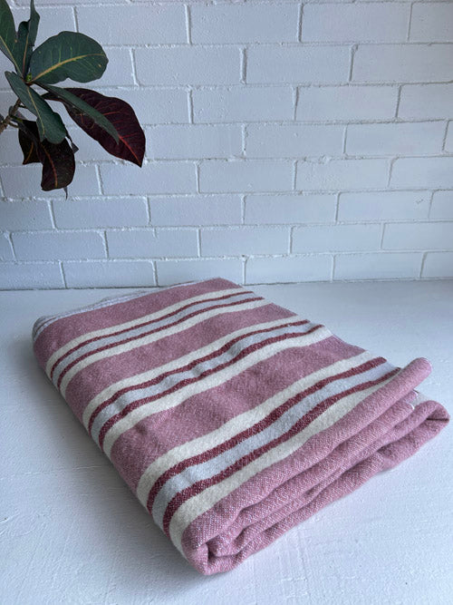 Folded pink and white striped towel on a white surface with a white brick wall background