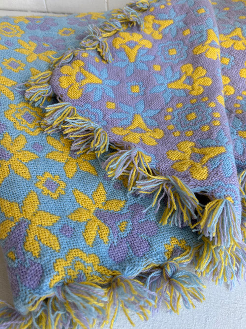 Multicolored textured blanket with floral patterns and tassels on a white background
