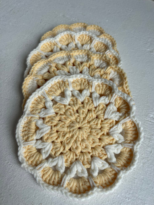 Set of four crocheted coasters with a beige and white pattern on a gray surface