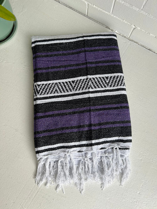 Striped Mexican Blanket with purple, black, and white pattern on a light gray surface.