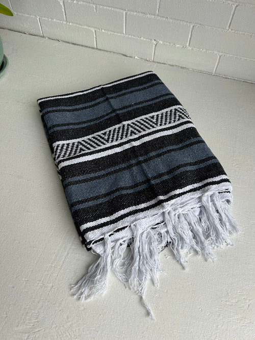 Blue, black and white striped Mexican blanket with fringes on a white surface