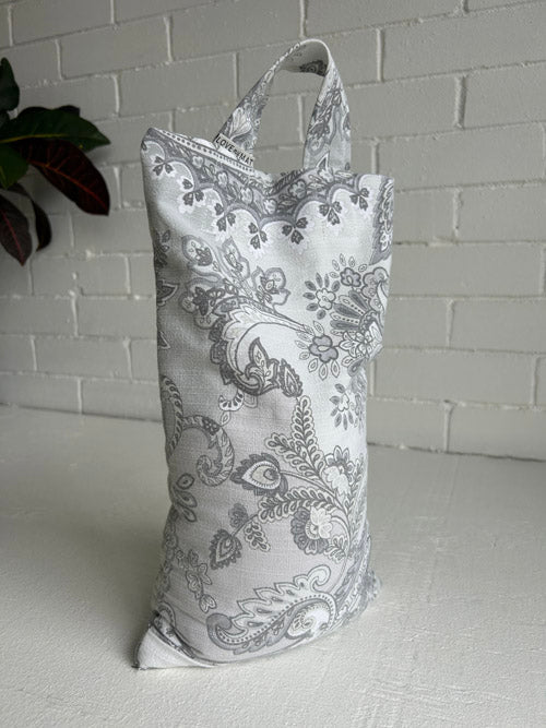 Fabric bag with paisley pattern on a white surface and light gray brick wall background
