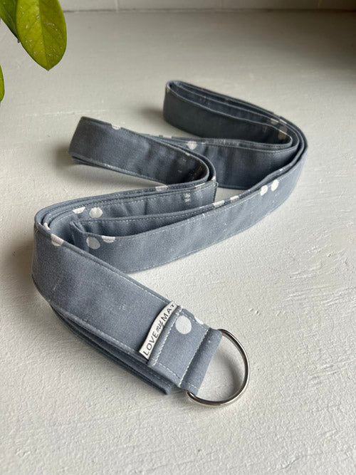 Gray yoga strap with a metal ring on a light gray surface