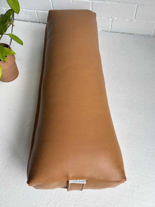 Brown Vinyl Yoga Bolster on a white surface with a plant in the background