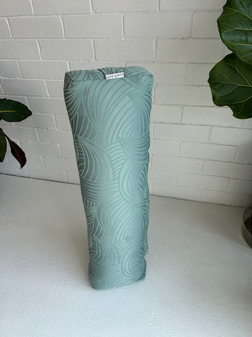 Green textured yoga bolster on a white surface with a white tiled wall background