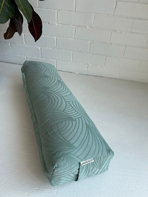 Green patterned sustainable yoga bolster on a white surface with a white brick wall background