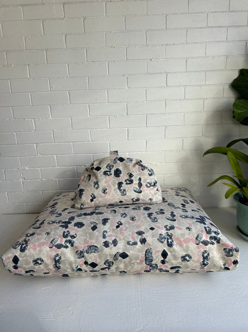 Modern brush stroke Meditation  cushion pet bed against a white brick wall with a plant on the right.