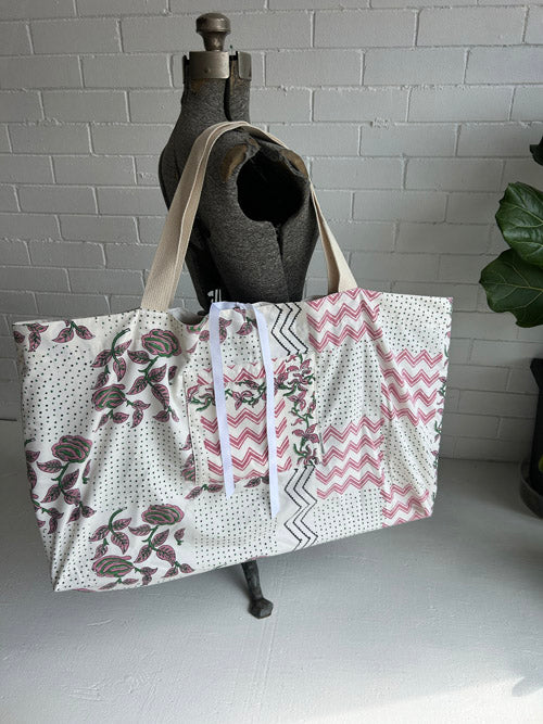 Patchwork tote bag with floral and zigzag patterns on a mannequin against a white brick wall.