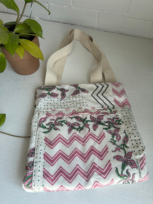 Tote bag with floral and zigzag pattern on a white surface with a plant in the background
