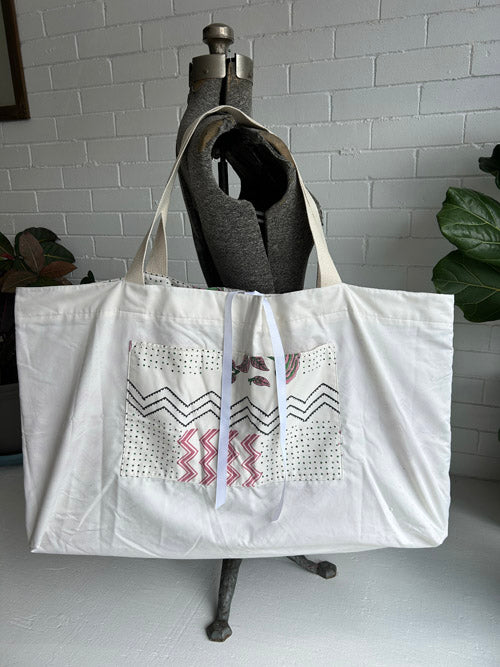 White tote bag with geometric patterns on a mannequin against a white tiled wall.