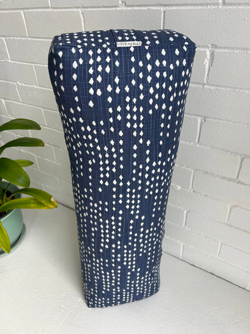 Navy blue and white patterned long yoga bolster on a white surface with a plant in the background