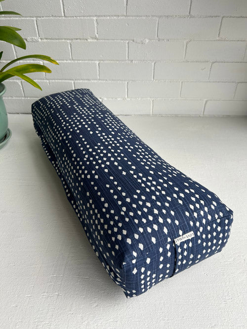 Navy blue yoga bolster with white patterns on a white surface with a white brick wall background.