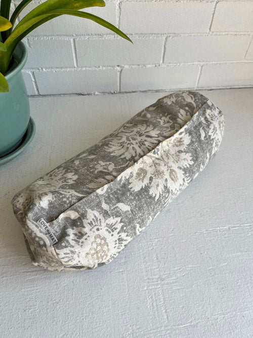 Neutral Coloured Fabric Mini round Yoga Bolster on a white surface and  white painted brick background.