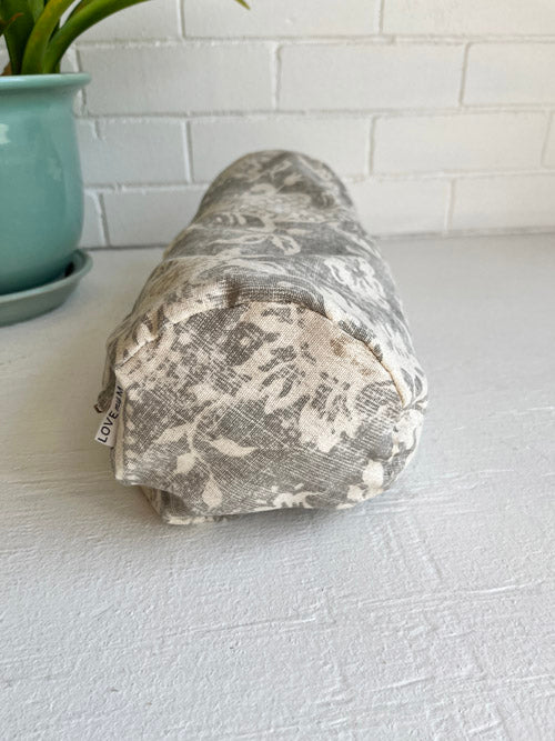 Neutral fabric mini round yoga bolster on a white surface with a plant in the background