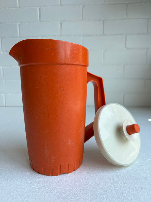Terracotta-colored pitcher with a white lid on a white surface.
