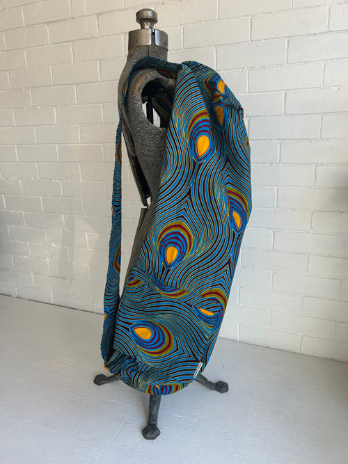 Colorful fabric yoga mat bag over a mannequin shoulder against a white brick wall.