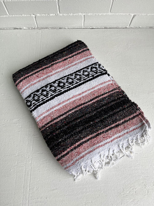 Woven blanket with black, pink, and white stripes on a white surface.