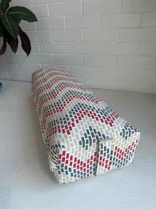 Patterned yoga bolster on a white surface with a white brick wall background