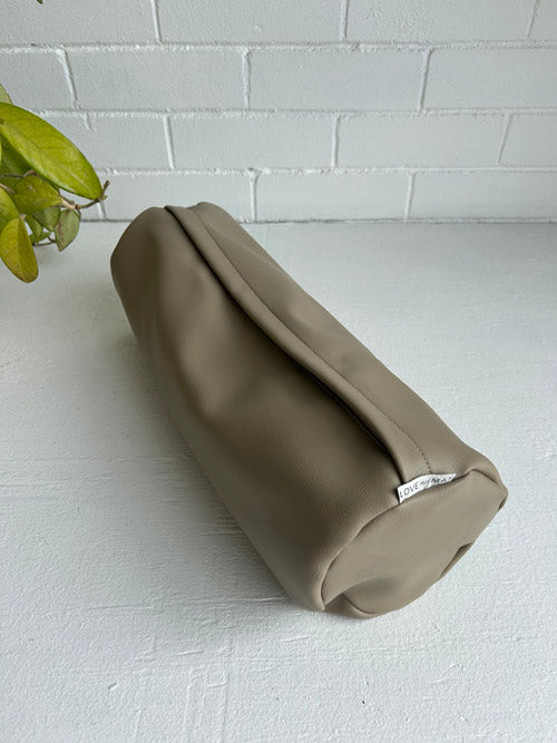 taupe colour mini round yoga bolster on a white surface and against a white backround